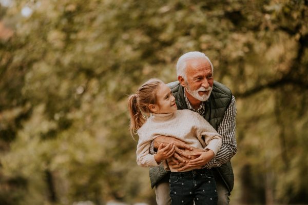 Grandfather spending time with his granddaughter in park on autumn day